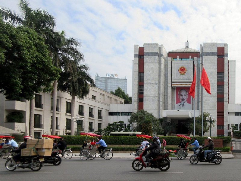 Giá đất hiện nay bao nhiêu 1m2? Bảng giá đất 2026 mới nhất Trụ sở UBND TP Hà Nội có quốc huy và cờ đỏ phía trước, xe máy chạy trên đường