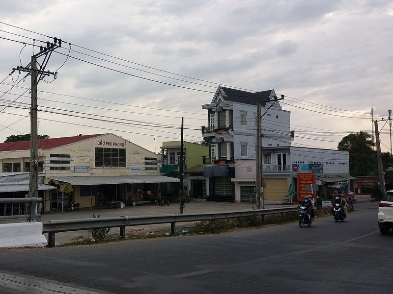 Bảng giá đất Đồng Tháp 2026 mới nhất: Tải bảng giá và cách tra giá Chợ Phú Phong mái đỏ cạnh nhà phố ba tầng bên đường, vài xe máy chạy qua